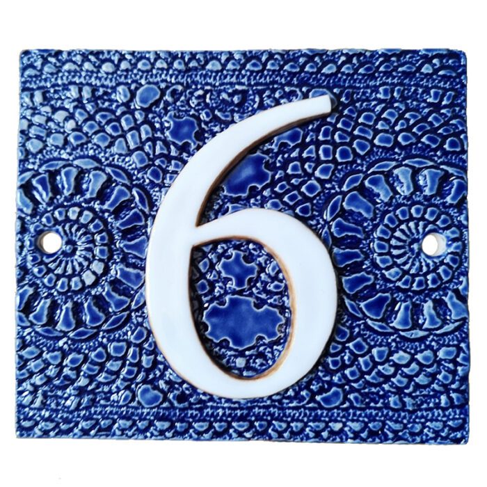 Huisnummer 6 in blauw met afdruk van een gehaakt kleedje als achtergrond